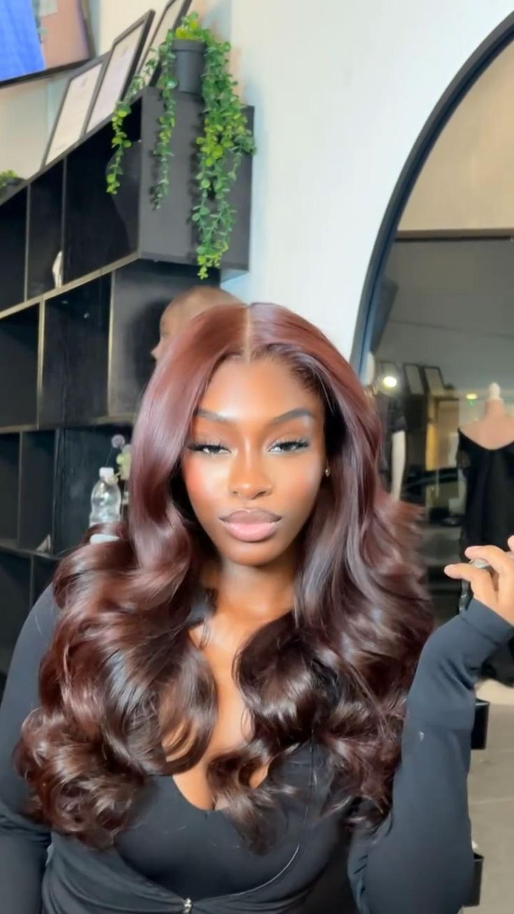 Model wearing a long reddish-brown wig with a centre part and loose curls.