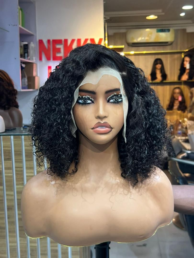 Black curly bob wig with visible untrimmed lace displayed on a mannequin in the shop.